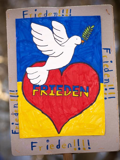 "FRIEDEN" steht auf einem Plakat. Außerdem ist ein rotes Herz und eine weiße Taube darauf zu sehen.