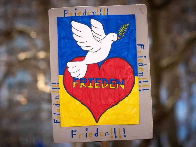 "FRIEDEN" steht auf einem Plakat. Außerdem ist ein rotes Herz und eine weiße Taube darauf zu sehen.
