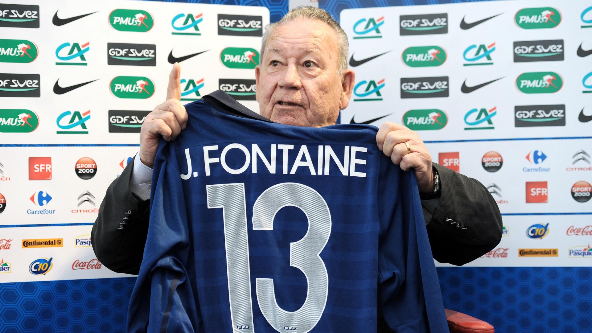 Das Foto zeigt den ehemaligen Fußball-Spieler Just Fontaine aus dem Land Frankreich. Er hält ein blaues Trikot mit dem Namen Fontaine und der Nummer 13 hoch. Das Foto zeigt den ehemaligen Fußball-Spieler Just Fontaine aus dem Land Frankreich. Er hält ein blaues Trikot mit dem Namen Fontaine und der Nummer 13 hoch.