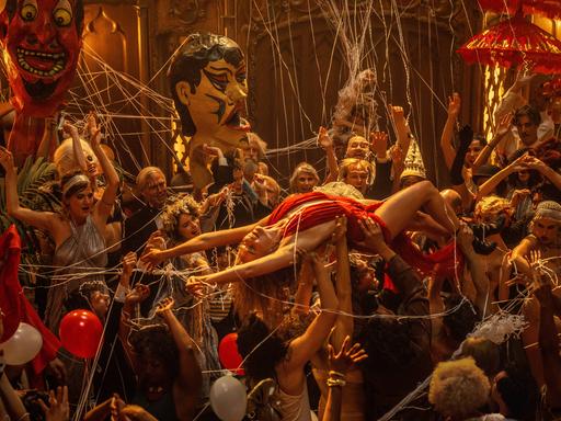 Filmstill aus "Babylon - Im Rausch der Ekstase": Auf dem Bild ist eine rauschhafte Bühnenszene zu sehen, bei der viele Schauspieler eine mit einem roten Kleid bekleidete Frau auf den Händen tragen und feiern.