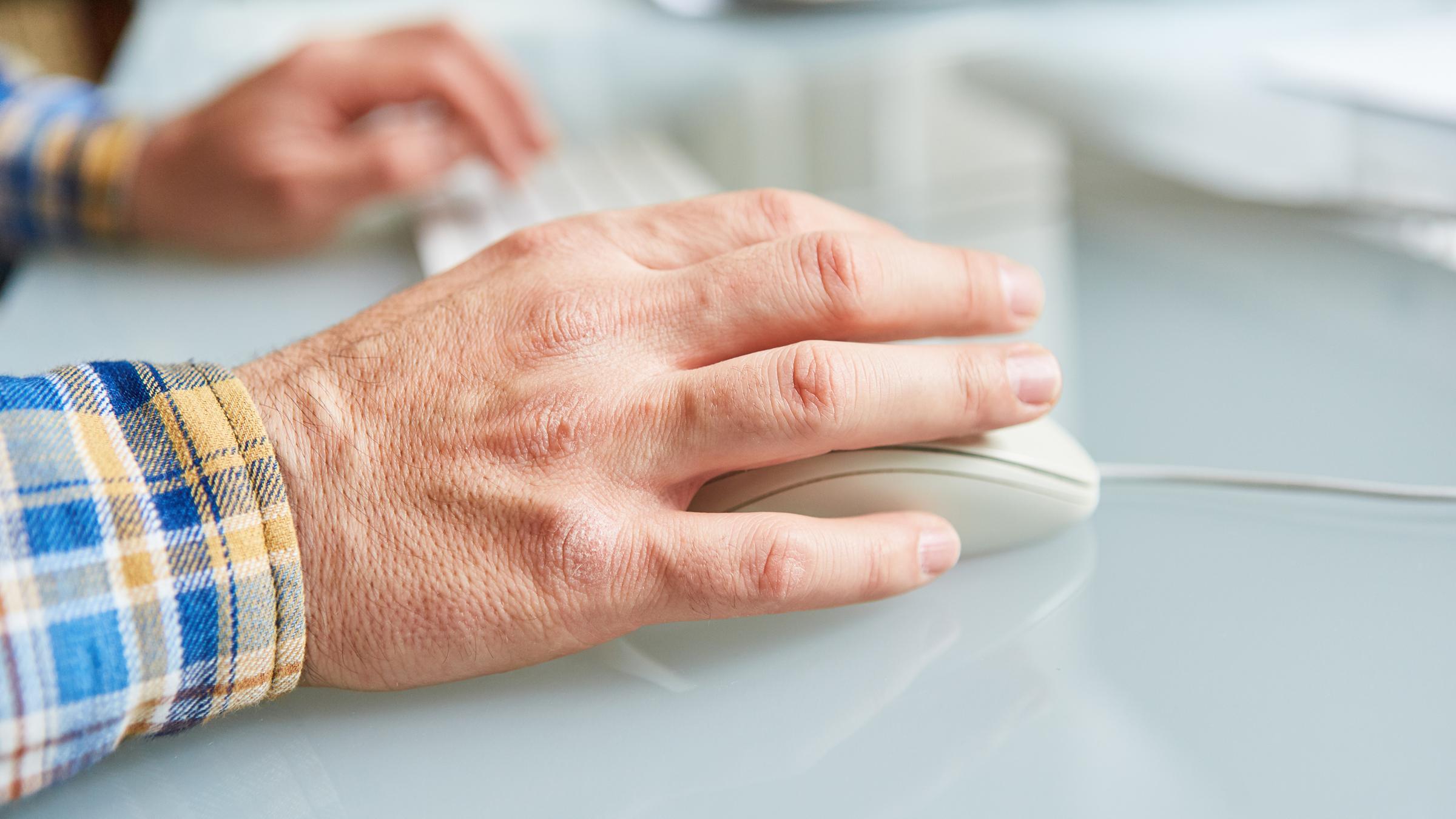 Eine Hand im Vordergrund bedient eine Computermaus. Die Hand im Hintergrund liegt auf der Computer-Tastatur. 