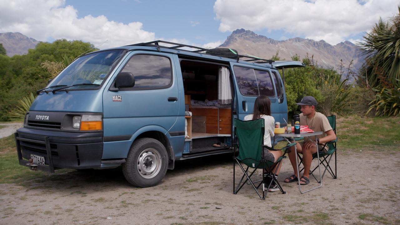 Zwei junge Camper frühstücken vor ihrem kleinen Bus in grüner Landschaft. Zwei junge Camper frühstücken vor ihrem kleinen Bus in grüner Landschaft.