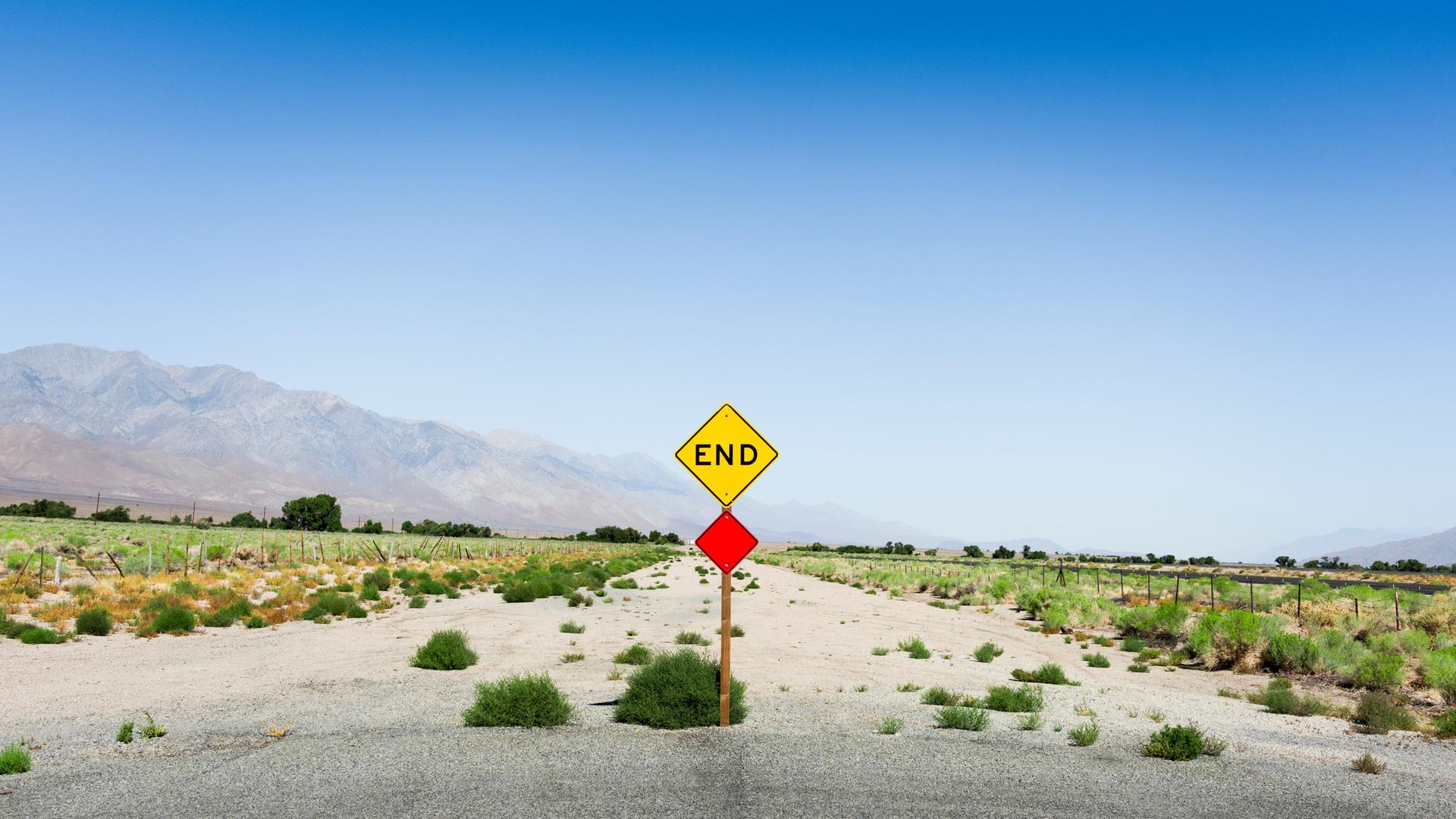 Ein Schotterweg endet in einer dürren Landschaft. Das Ende des Weges ist mit einem gelben Schild markiert, das die Aufschrift "End" trägt. Ein Schotterweg endet in einer dürren Landschaft. Das Ende des Weges ist mit einem gelben Schild markiert, das die Aufschrift "End" trägt.