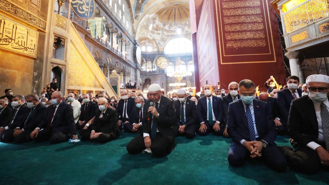 Präsident Erdogan kniet mit bedecktem Kopf auf dem türkisfarbenen Teppich der Hagia Sophia inmitten vieler anderer Männer auf Knien und mit Krawatten. Präsident Erdogan kniet mit bedecktem Kopf auf dem türkisfarbenen Teppich der Hagia Sophia inmitten vieler anderer Männer auf Knien und mit Krawatten.
