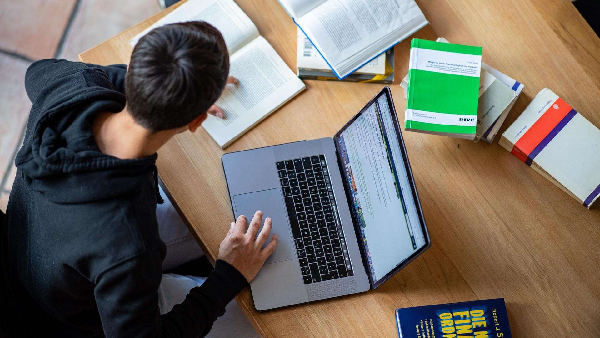 Ein Student sitzt vor einem Laptop im Wohnzimmer und blickt auf die Webseite der Uni in Köln, Aufnahme von oben Ein Student sitzt vor einem Laptop im Wohnzimmer und blickt auf die Webseite der Uni in Köln, Aufnahme von oben