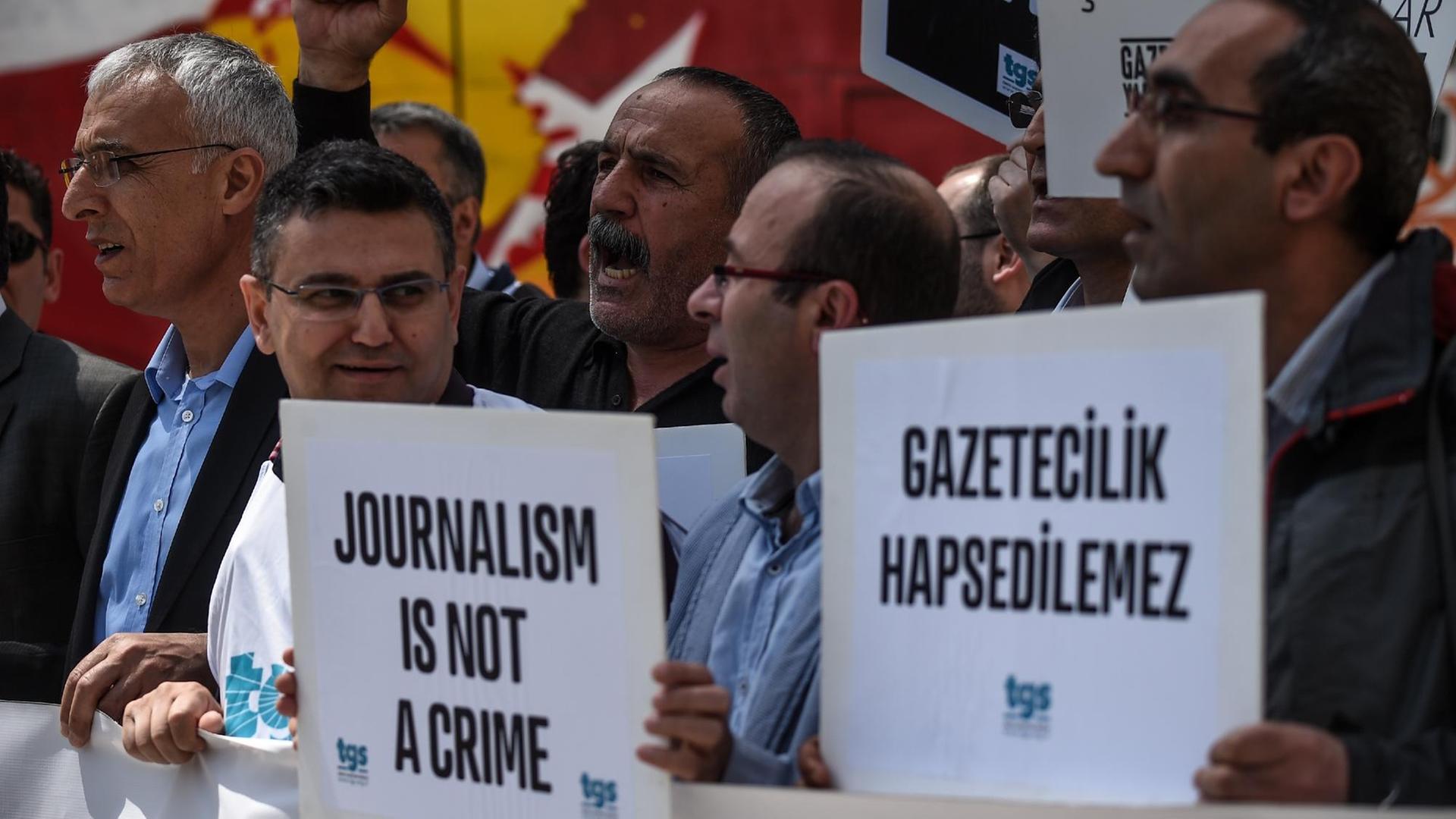 Mehrere Männer stehen in einer Menge, einige halten Plakate mit der Aufschrift "Journalismus ist kein Verbrechen". Mehrere Männer stehen in einer Menge, einige halten Plakate mit der Aufschrift "Journalismus ist kein Verbrechen".