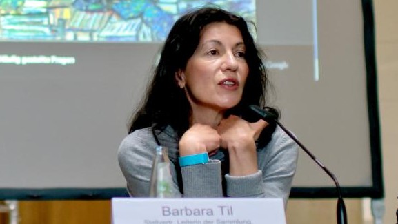 Barbara Til sitzt hinter einem Schild mit ihrem Namen. Barbara Til sitzt hinter einem Schild mit ihrem Namen.