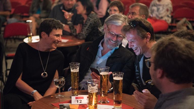 An diesem Abend noch im Publikum, am nächsten selbst auf der Bühne: Lisa Oberzaucher, Helmut Jungwirth und weitere Mitglieder von Sience Busters sitzen lachend im Publikum und schauen gemeinsam auf ein Handydisplay. An diesem Abend noch im Publikum, am nächsten selbst auf der Bühne: Lisa Oberzaucher, Helmut Jungwirth und weitere Mitglieder von Sience Busters sitzen lachend im Publikum und schauen gemeinsam auf ein Handydisplay.