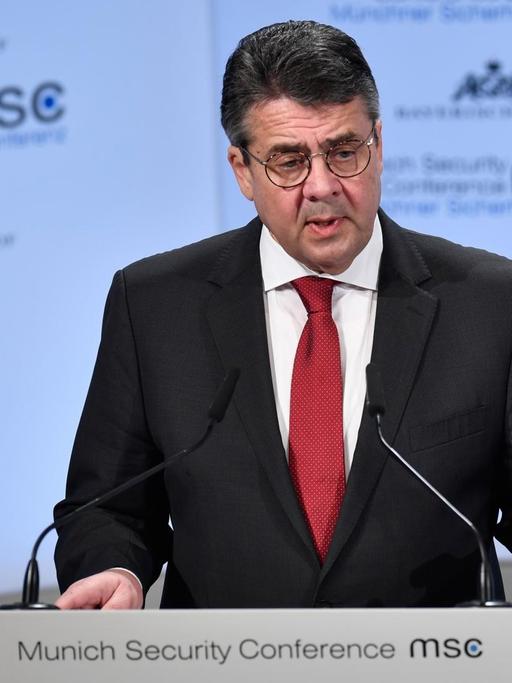 Bundesaußenminister Gabriel bei seiner Rede auf der Münchner Sicherheitskonferenz 2018. Er steht an einen Pult mit Mikrophonen, dahinter eine Wand mit Logos der Konferenz.