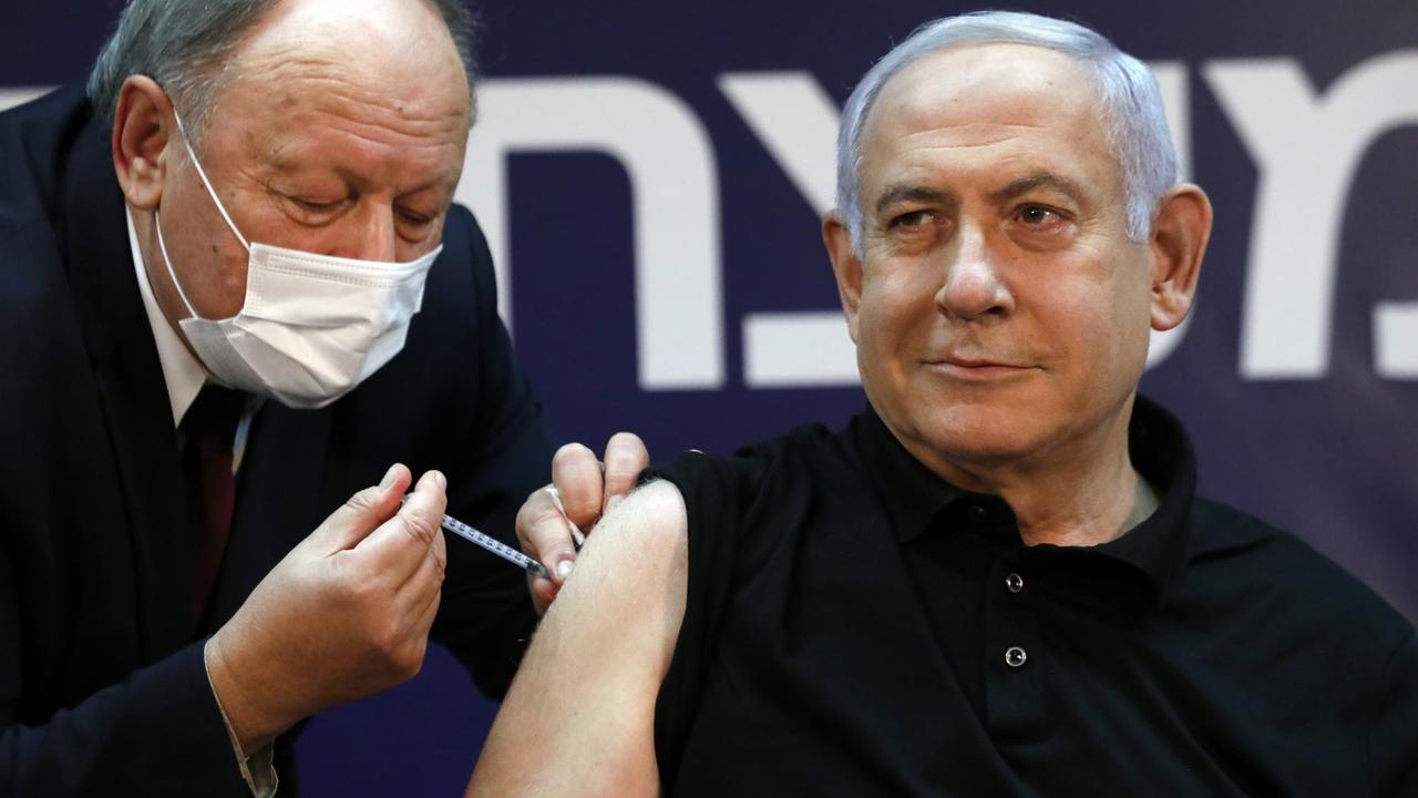 Netanjahu lächelt milde, während ihm ein Arzt mit Mundschutz das Serum injiziert.