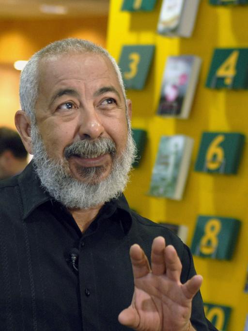 Der kubanische Schriftsteller Leonardo Padura gestikuliert und spricht. Hinter ihm sind Regale mit Büchern.