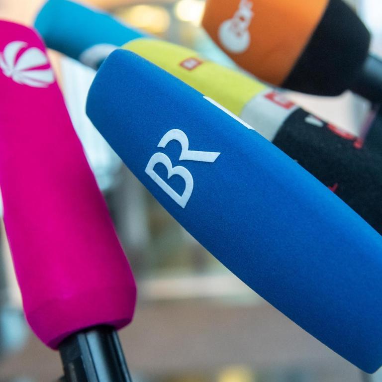 Diverse Mikrofone von öffentlichen und privaten Fernsehsendern stehen zu Beginn einer Pressekonferenz nebeneinander.
