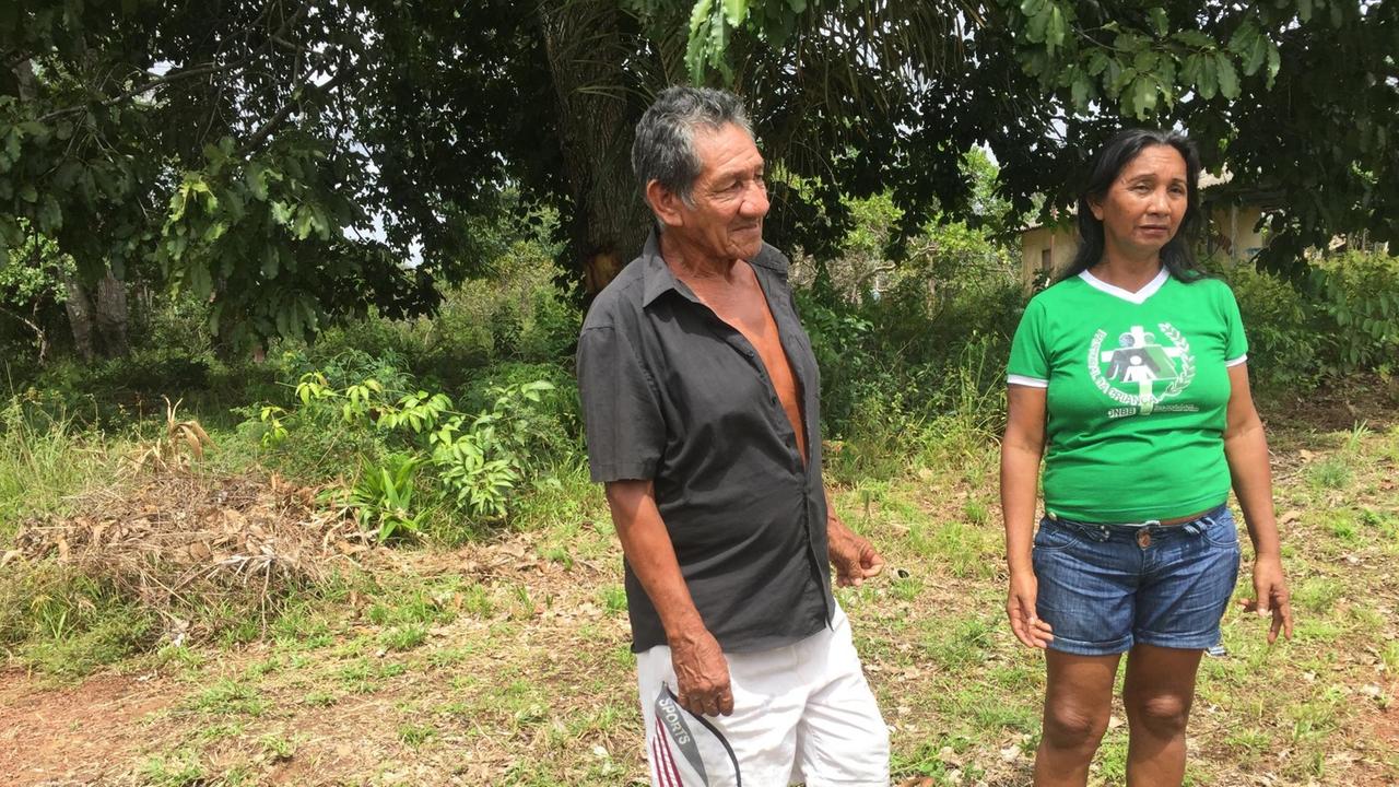 Gemeindeleiterin Amelia Praga Cabral im knallgrünen T-Shirt und kurzen Jeans steht mit einem Mann vor einem Wald auf einer Wiese. Gemeindeleiterin Amelia Praga Cabral im knallgrünen T-Shirt und kurzen Jeans steht mit einem Mann vor einem Wald auf einer Wiese.