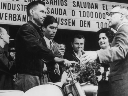 Der millionste Gastarbeiter in der Bundesrepublik, Armando Rodrigues (l.) aus Portugal, steht neben dem Moped, das er bei seiner Ankunft am 10.09.1964 im Köln-Deutzer Bahnhof geschenkt bekam.
