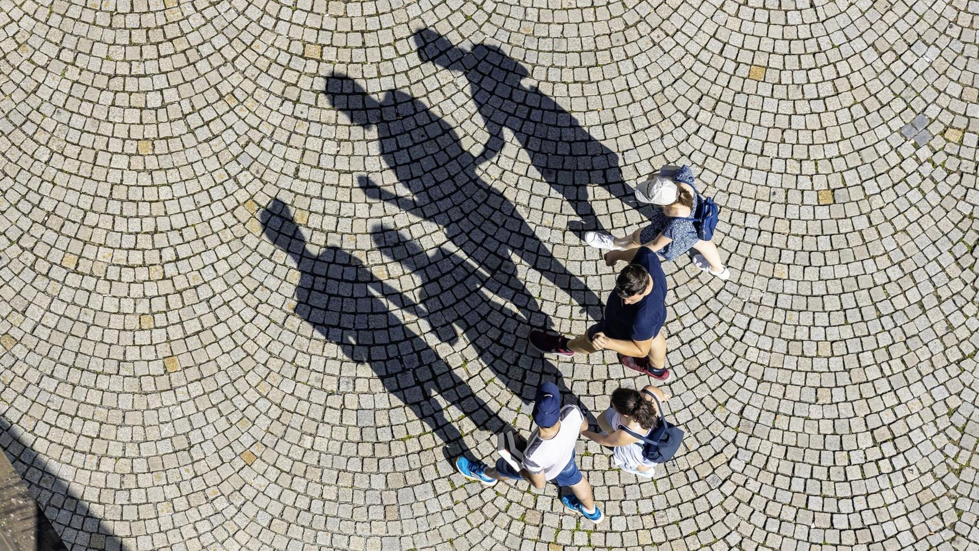 Vier Menschen aus der Vogelperspektive werfen Schatten aufs Kopfsteinplaster