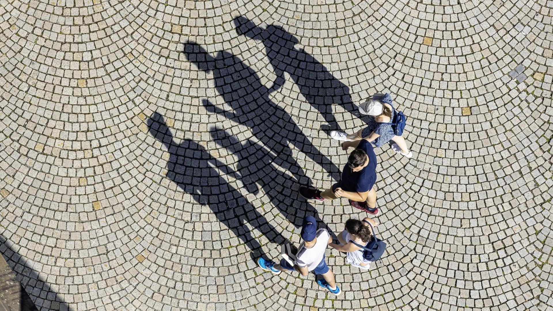 Vier Menschen aus der Vogelperspektive werfen Schatten aufs Kopfsteinplaster Vier Menschen aus der Vogelperspektive werfen Schatten aufs Kopfsteinplaster