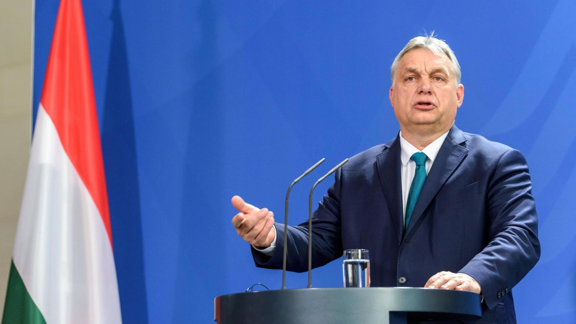 Viktor Orbán steht an einem Redner-Pult, neben ihm hängt die ungarische Flagge: rot-weiß-grün. Viktor Orbán steht an einem Redner-Pult, neben ihm hängt die ungarische Flagge: rot-weiß-grün.