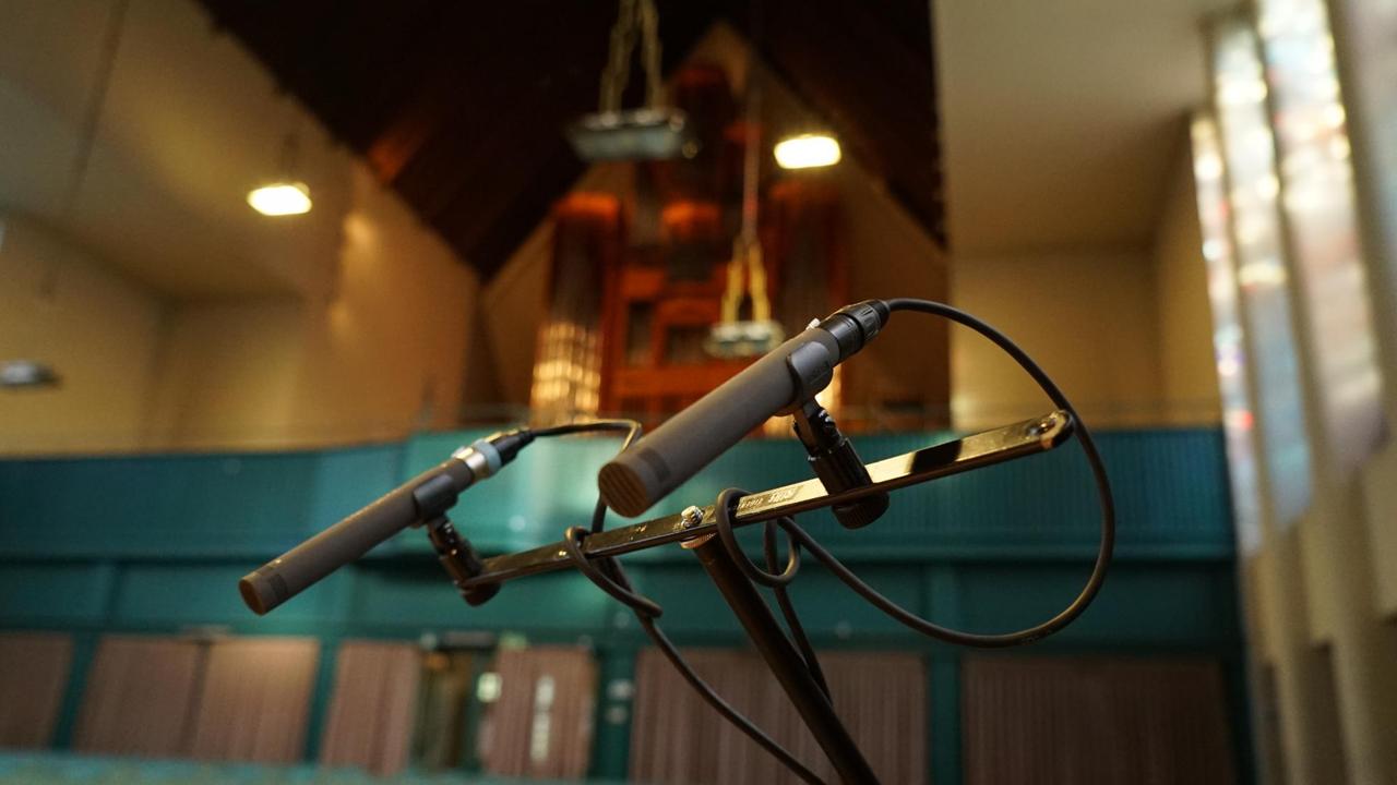 Ein Mikrophonständer in einem Kirchenraum, in dessen Hintergrund eine Orgel sichtbar ist. Ein Mikrophonständer in einem Kirchenraum, in dessen Hintergrund eine Orgel sichtbar ist.
