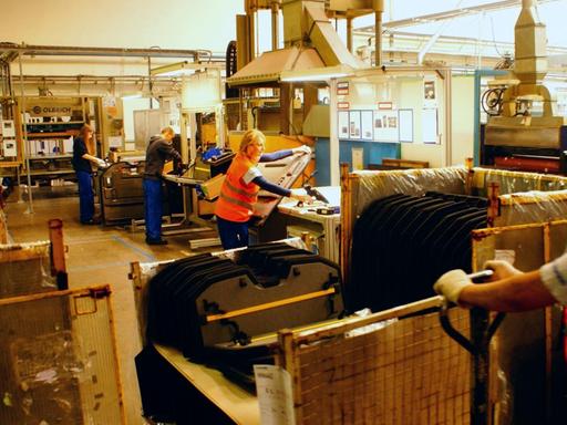 Mehrere Arbeiter in einer Fabrikhallte stehen an ihren Maschinen.
