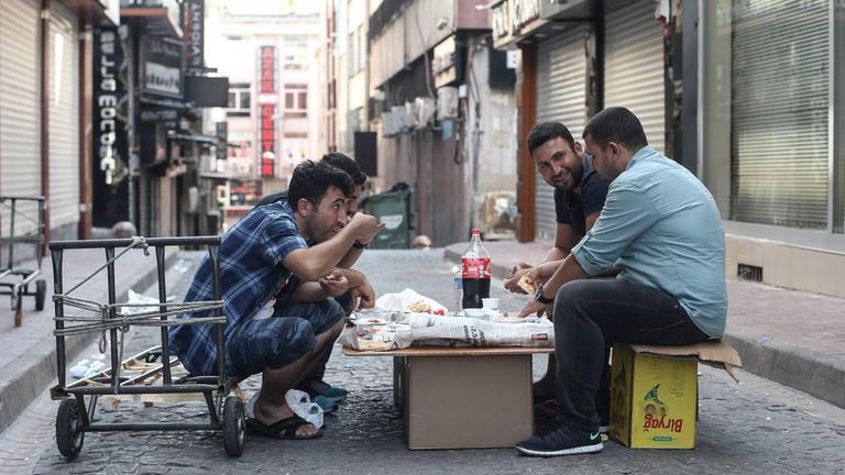 Syrische Flüchtlinge sitzen in eine Gasse in Istanbul an einem Tisch aus Pappkartons auf der Straße und essen etwas. 