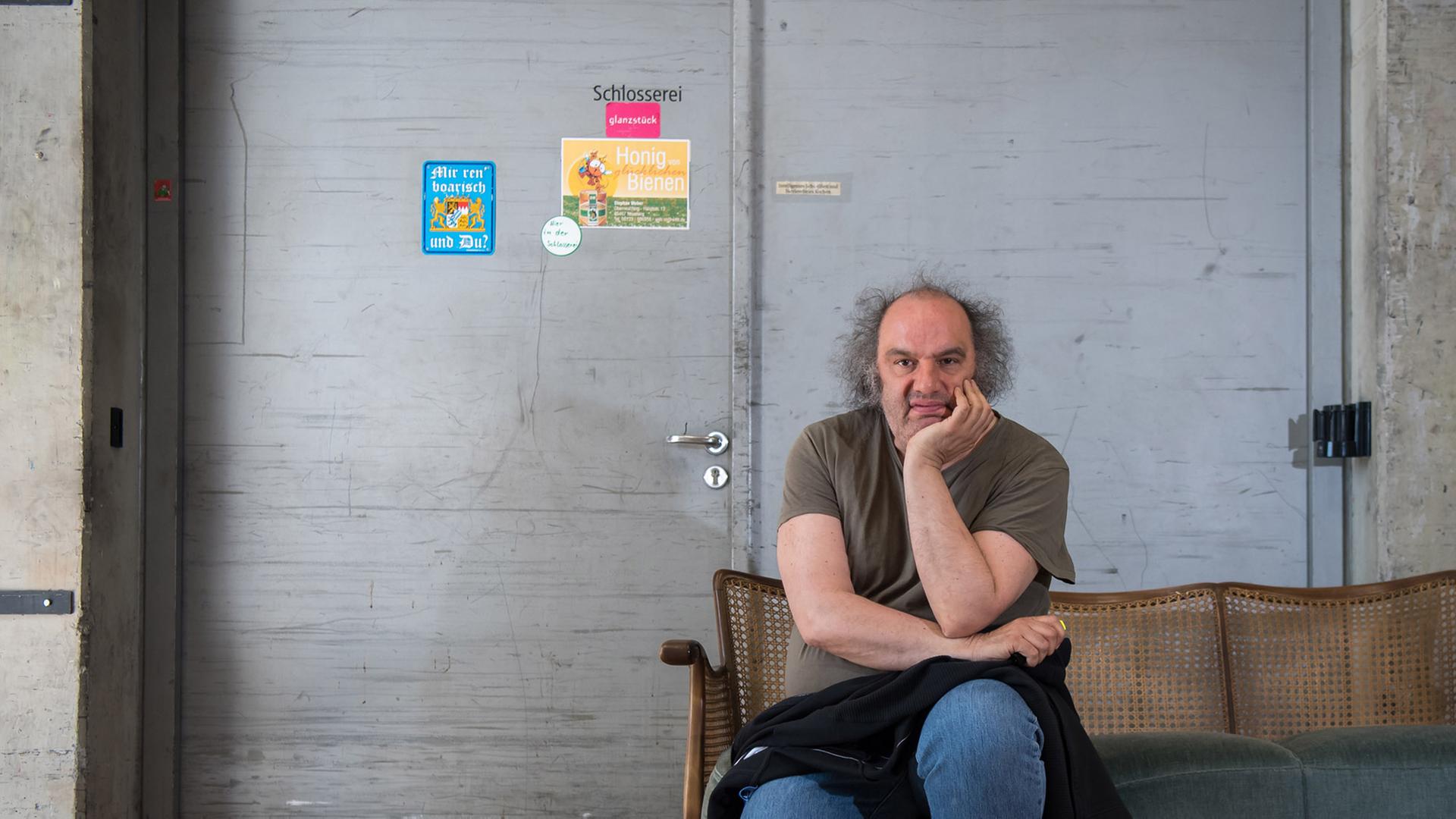 Matthias Lilienthal, Intendant der Münchner Kammerspiele, sitzt auf einem Sofa vor einer Stahltür mit der Aufschrift Schlosserei.