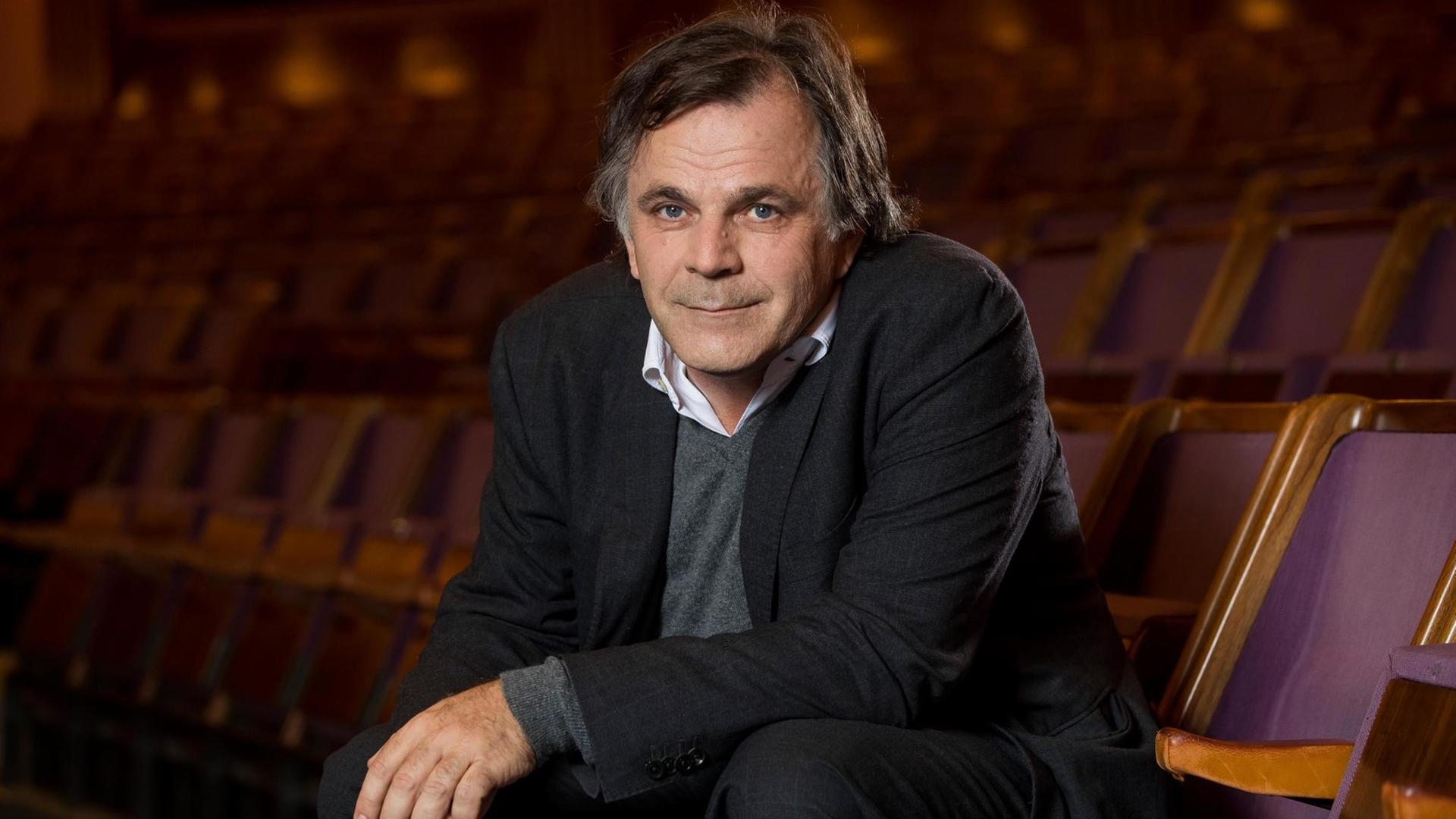 Das Bild zeigt Markus Hinterhäuser, sitzend in einem Zuschauersaal mit violetten Samitsesseln Das Bild zeigt Markus Hinterhäuser, sitzend in einem Zuschauersaal mit violetten Samitsesseln