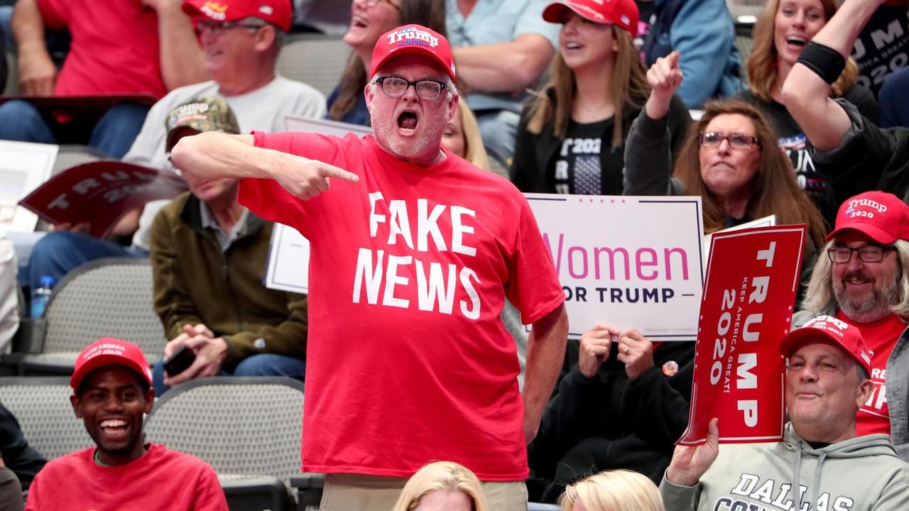Ein Donald Trump Fan bei "Keep America Great" in Dallas, er trägt eine rotes T-Shirt mit dem Schriftzug "Fake News", Texas, 2019. Ein Donald Trump Fan bei "Keep America Great" in Dallas, er trägt eine rotes T-Shirt mit dem Schriftzug "Fake News", Texas, 2019.
