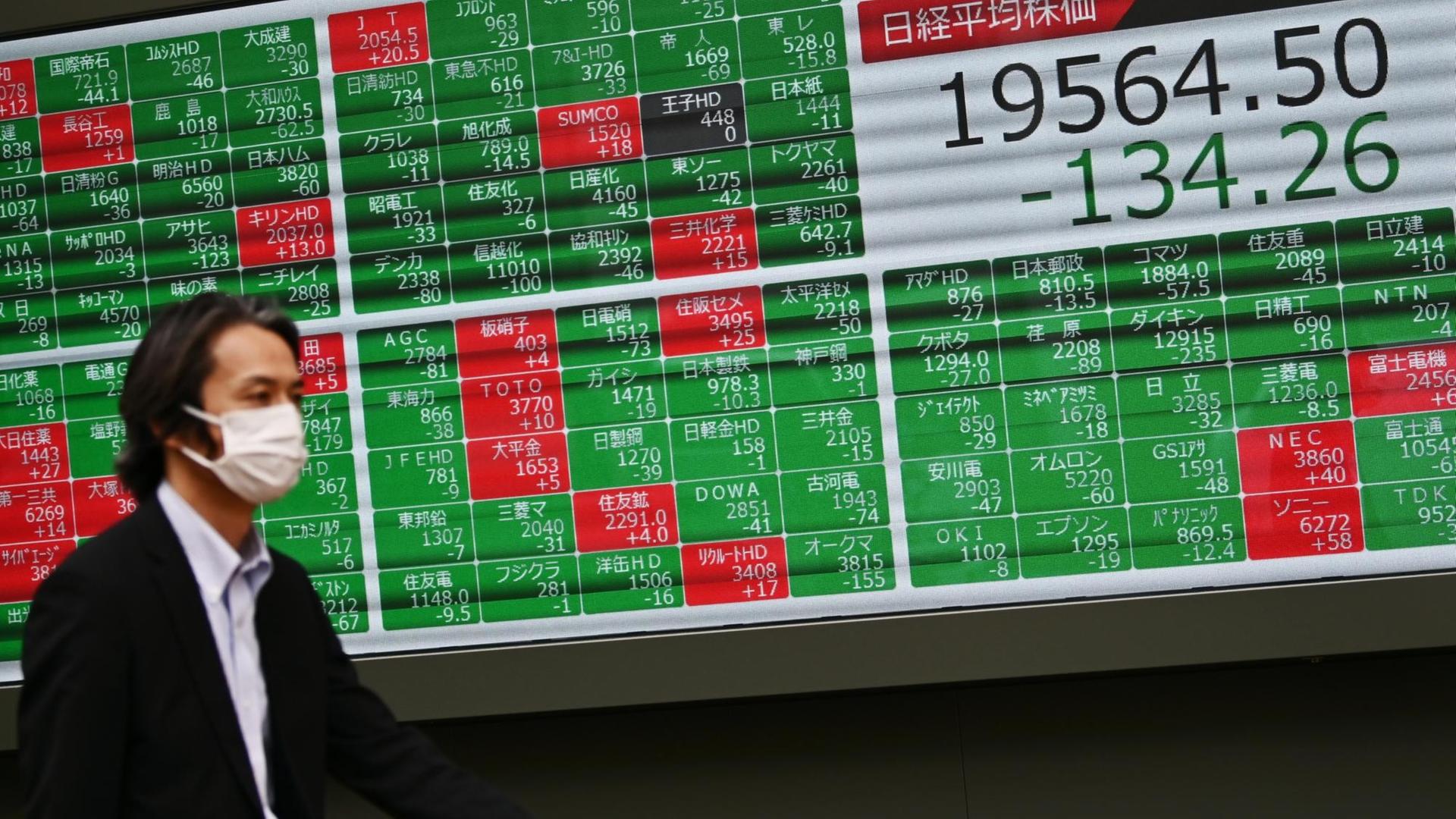 Ein Fußgänger mit einem Mundschutz geht in Tokio an einer Leuchttafel mit Börsennotierungen vorbei Ein Fußgänger mit einem Mundschutz geht in Tokio an einer Leuchttafel mit Börsennotierungen vorbei