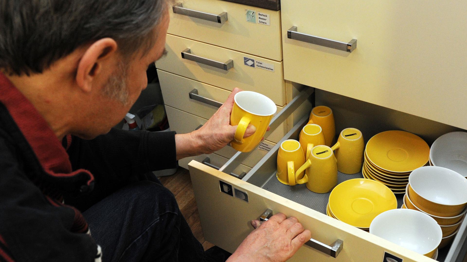 Ein Mann nimmt sich eine gelbe Tasse aus dem Schrank Ein Mann nimmt sich eine gelbe Tasse aus dem Schrank