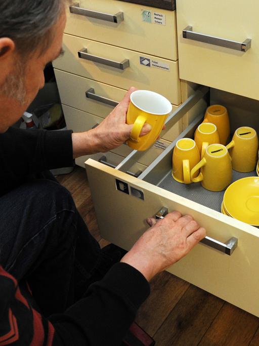 Ein Mann nimmt sich eine gelbe Tasse aus dem Schrank