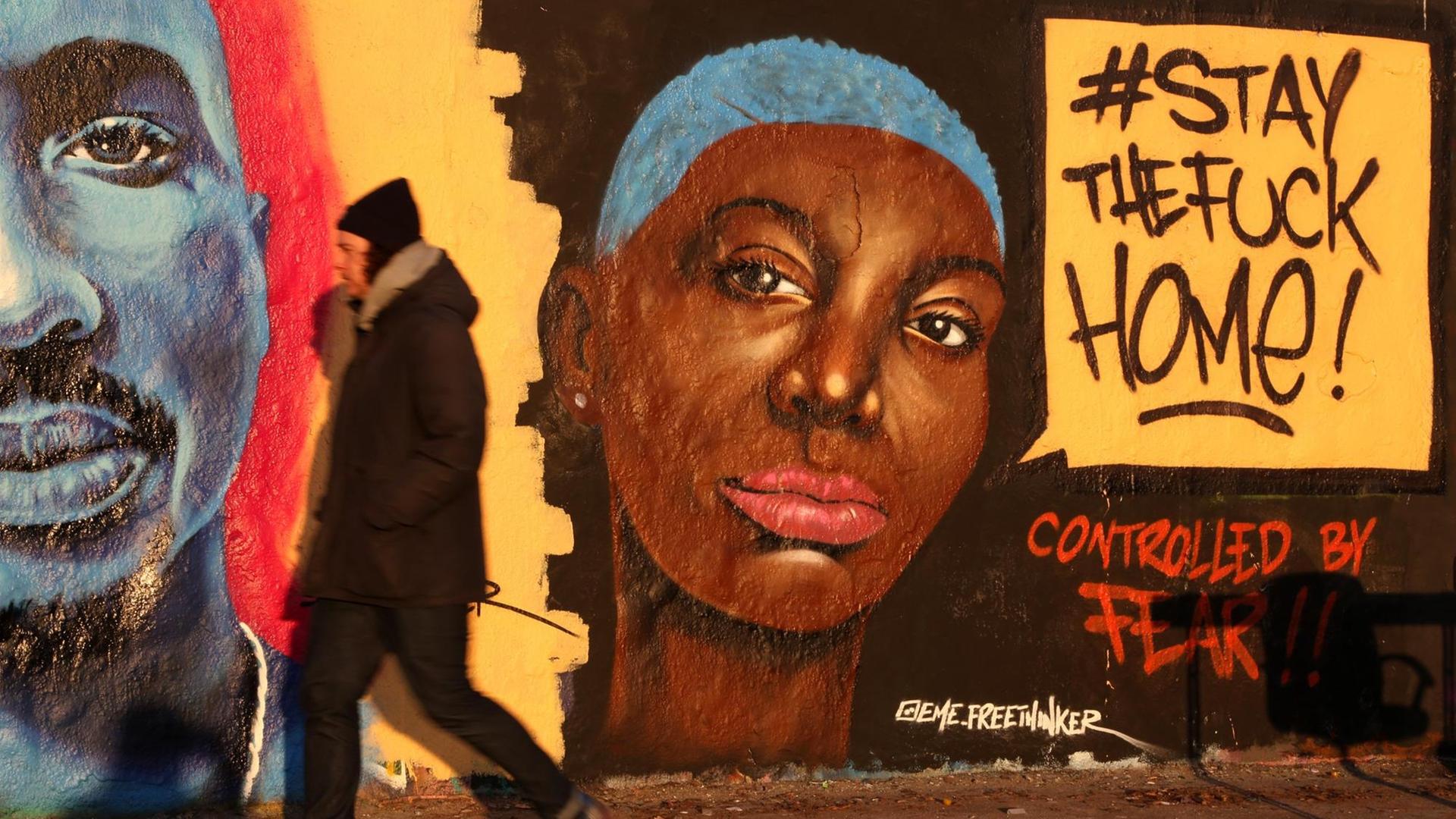 Ein Mann geht an einem Graffito vorbei, das eine Frau mit strengem Blick und einer Sprechblase zeigt: '#stay the fuck home!' Darunter steht: 'Controlled by fear.' Zu Deutsch: Bleibt gefälligst zu Hause! Von der Angst kontrolliert. Ein Mann geht an einem Graffito vorbei, das eine Frau mit strengem Blick und einer Sprechblase zeigt: '#stay the fuck home!' Darunter steht: 'Controlled by fear.' Zu Deutsch: Bleibt gefälligst zu Hause! Von der Angst kontrolliert.