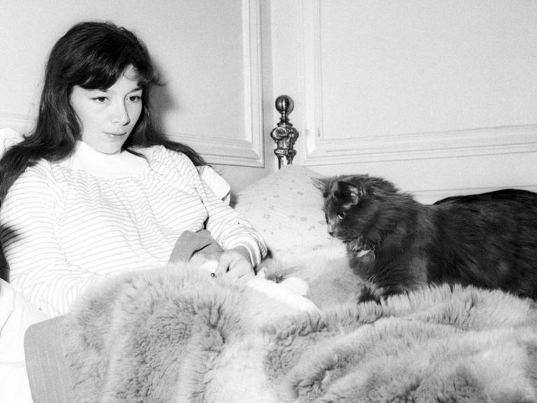 Schwarz-weiß Bild: Juliette Gréco (1954) sitzt im Bett. Neben ihr liegt eine Katze.