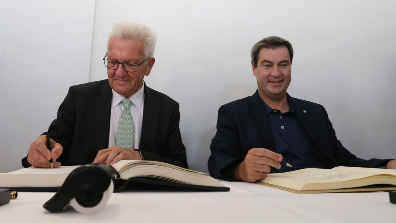 23.07.2019, Baden-Württemberg, Meersburg: Winfried Kretschmann, Ministerpräsident von Baden-Württemberg (Grüne,l) und Markus Söder, bayerischer Ministerpräsident (CSU) tragen sich in die Bücher der Stadt und des Landes ein. Foto: Karl-Josef Hildenbrand/dpa | Verwendung weltweit 23.07.2019, Baden-Württemberg, Meersburg: Winfried Kretschmann, Ministerpräsident von Baden-Württemberg (Grüne,l) und Markus Söder, bayerischer Ministerpräsident (CSU) tragen sich in die Bücher der Stadt und des Landes ein. Foto: Karl-Josef Hildenbrand/dpa | Verwendung weltweit
