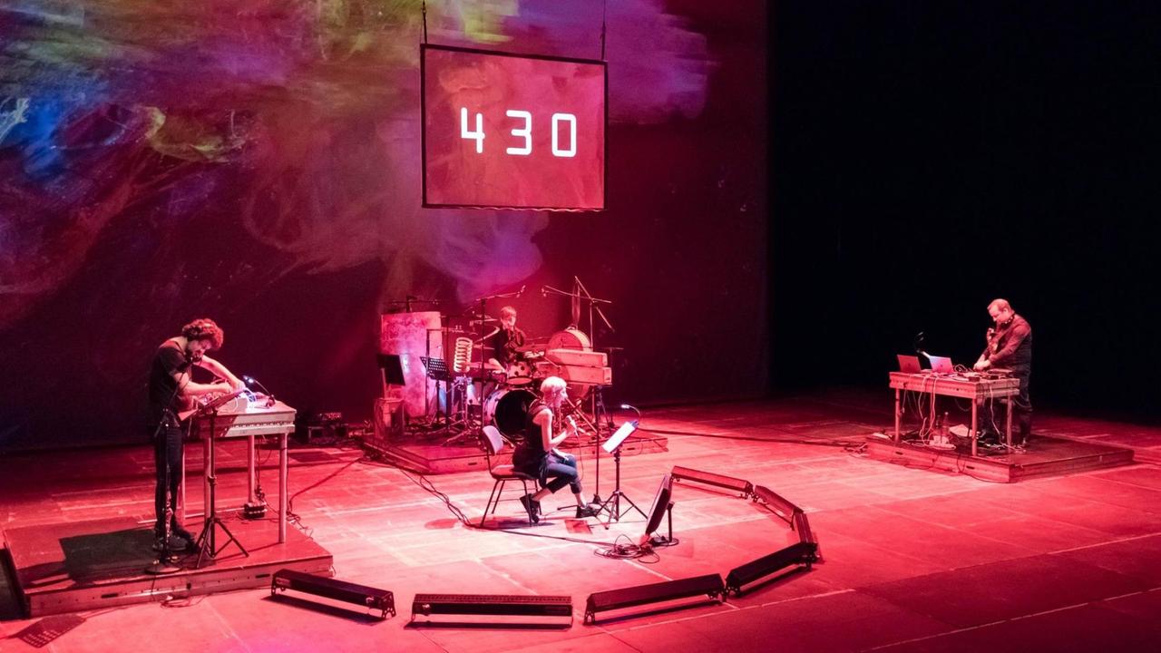 v.l.: Oguz Büyükberber (Klarinette, Elektronik), Jelena Kuljic (Stimme, Performance), Daniel Eichholz (Schlagzeug) und Marc Sinan (Komposition, E-Gitarre, Elektronik) interpretieren "The Number of the Beast" im Radialsystem V, Berlin vor einer Videoleinwand, darauf sind im rötlichen Licht weiß die Ziffern "430" zu sehen v.l.: Oguz Büyükberber (Klarinette, Elektronik), Jelena Kuljic (Stimme, Performance), Daniel Eichholz (Schlagzeug) und Marc Sinan (Komposition, E-Gitarre, Elektronik) interpretieren "The Number of the Beast" im Radialsystem V, Berlin vor einer Videoleinwand, darauf sind im rötlichen Licht weiß die Ziffern "430" zu sehen