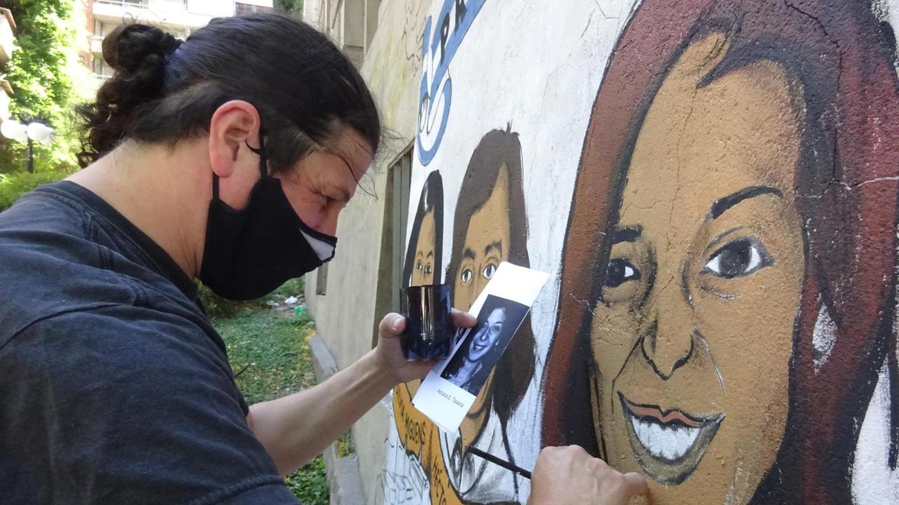 Ein Mann mit dunklen Haaren und dunklem T-Shirt malt ein Graffiti, das eine Frau darstellt. In der linken Hand hält er ein Foto der Frau. Ein Mann mit dunklen Haaren und dunklem T-Shirt malt ein Graffiti, das eine Frau darstellt. In der linken Hand hält er ein Foto der Frau.