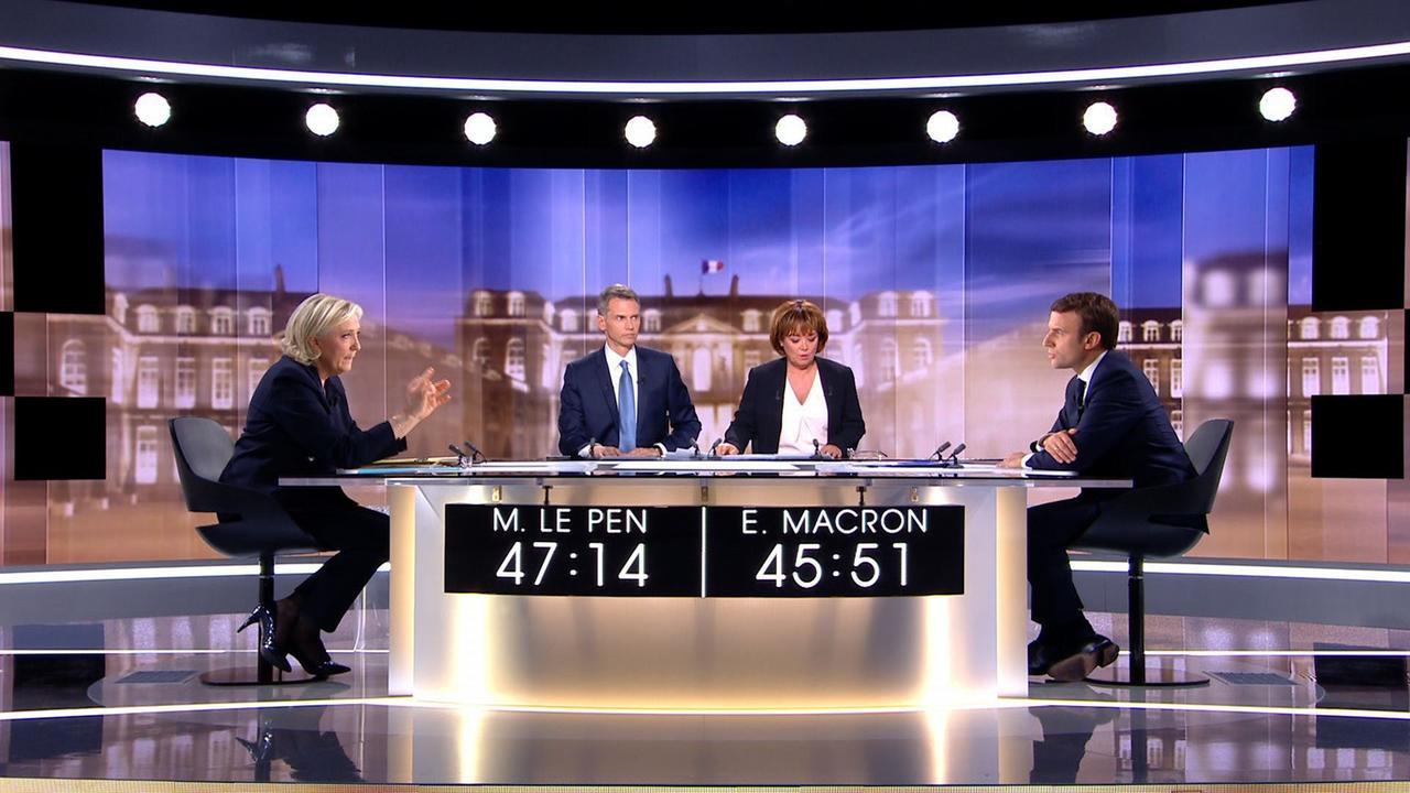Marine Le Pen und Emmanuel Macron sitzen sich in einem Fernsehstudio an einem runden Tisch gegenüber. Dazwischen die beiden Moderatoren. Marine Le Pen und Emmanuel Macron sitzen sich in einem Fernsehstudio an einem runden Tisch gegenüber. Dazwischen die beiden Moderatoren.