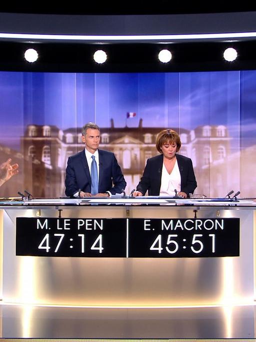 Marine Le Pen und Emmanuel Macron sitzen sich in einem Fernsehstudio an einem runden Tisch gegenüber. Dazwischen die beiden Moderatoren.