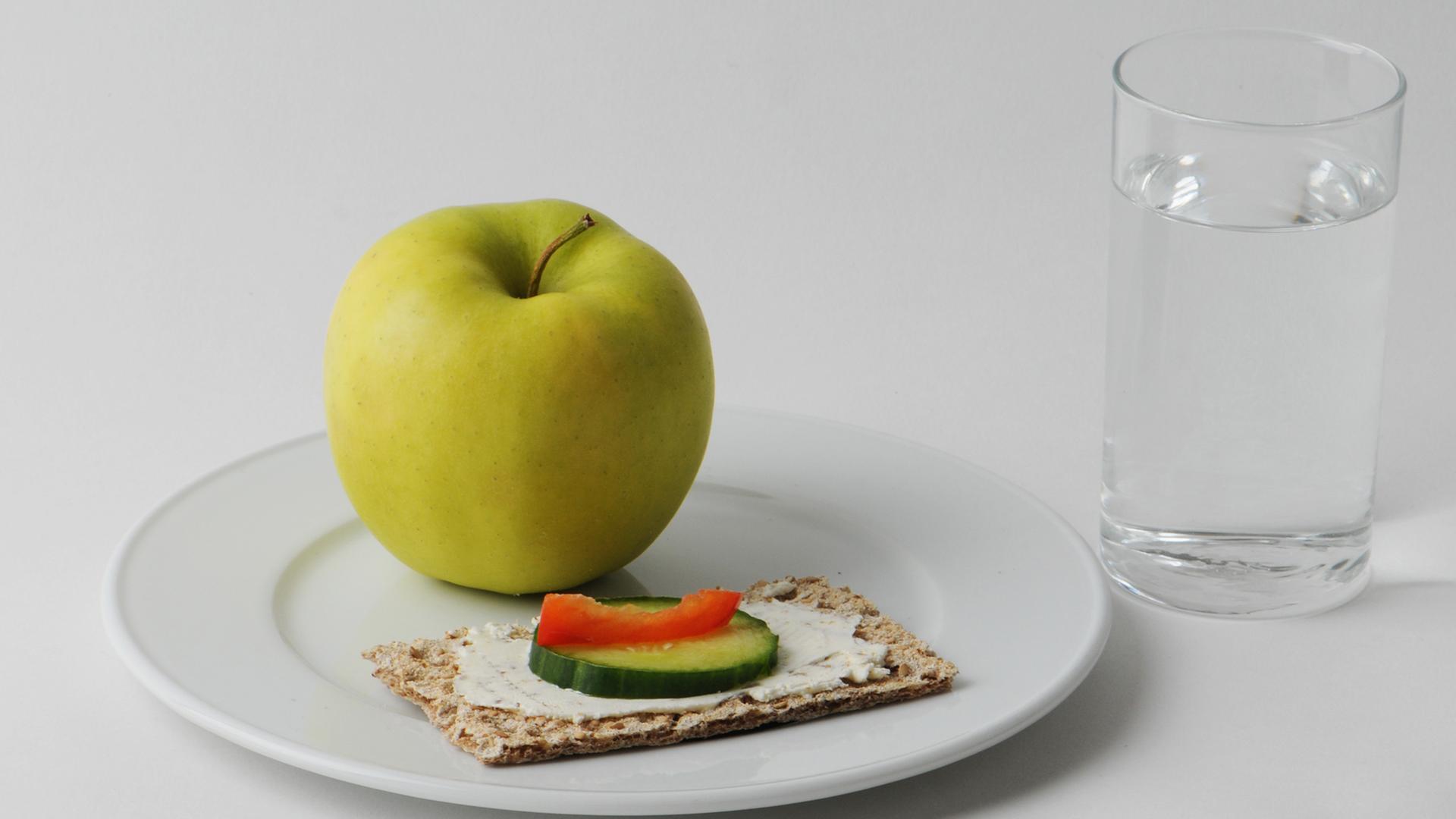 Ein Apfel und ein Knäckebrot neben einem Glas Wasser.