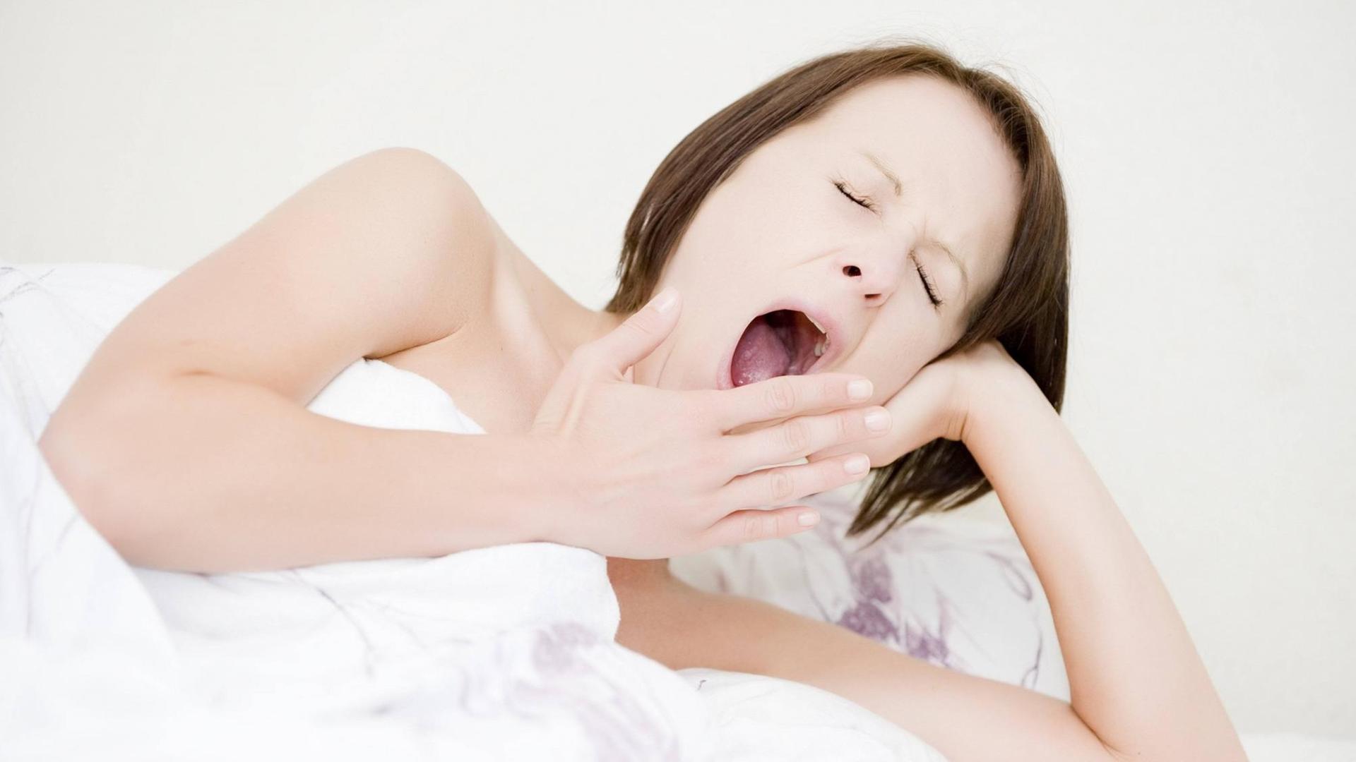Eine Frau liegt im Bett und gähnt. Eine Frau liegt im Bett und gähnt.