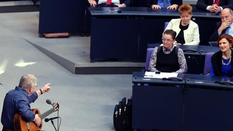 Der Liedermacher Wolf Biermann singt am 07.11.2014 während einer Gedenkveranstaltung zum 25. Jahrestag des Mauerfalls im Deutschen Bundestag in Berlin. Im Hintergrund verfolgt Richard Pitterle (3. Reihe, mitte) der Linken den Vortrag.