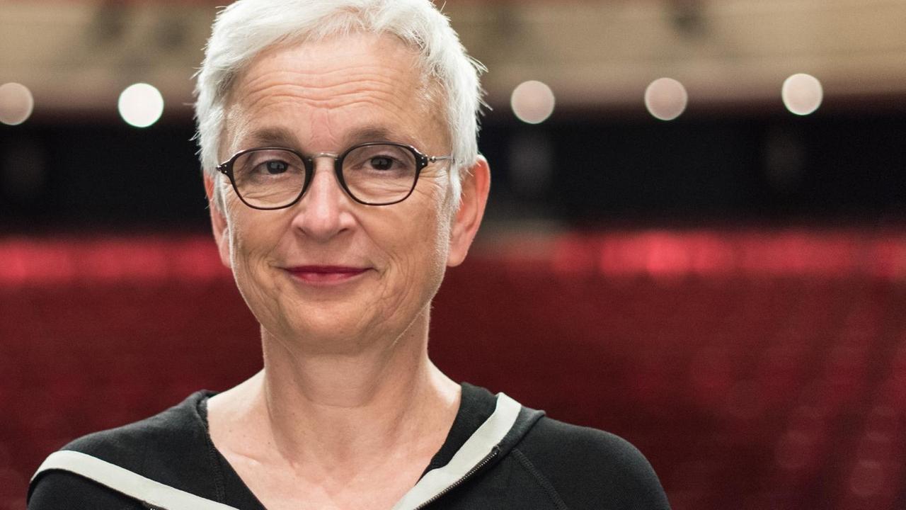 Barbara Mundel steht im Theater Freiburg und trägt kurze Haare und eine schwarze Brille