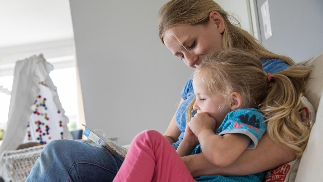 Eine Mutter liest ihrer Tochter auf der Couch etwas vor Eine Mutter liest ihrer Tochter auf der Couch etwas vor