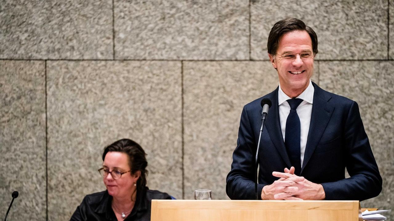 Premierminister Mark Rutte steht während einer Debatte im Parlament an einem Rednerpult, hinter ihm sitzt die Ministerin Tamara van Ark für medizinische Versorgung. Premierminister Mark Rutte steht während einer Debatte im Parlament an einem Rednerpult, hinter ihm sitzt die Ministerin Tamara van Ark für medizinische Versorgung.