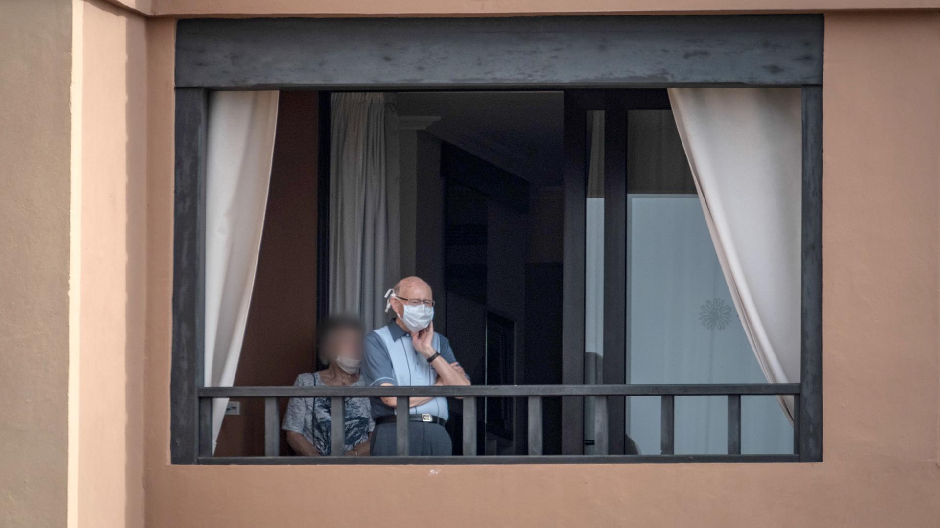 Ältere Leute stehen mit Mundschutz auf einem Balkon des Hotels H10 Costa Adeje Palace. Ältere Leute stehen mit Mundschutz auf einem Balkon des Hotels H10 Costa Adeje Palace.