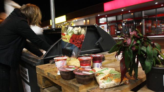 Eine Frau wühlt in einem Container nach weggeworfenen Lebensmitteln