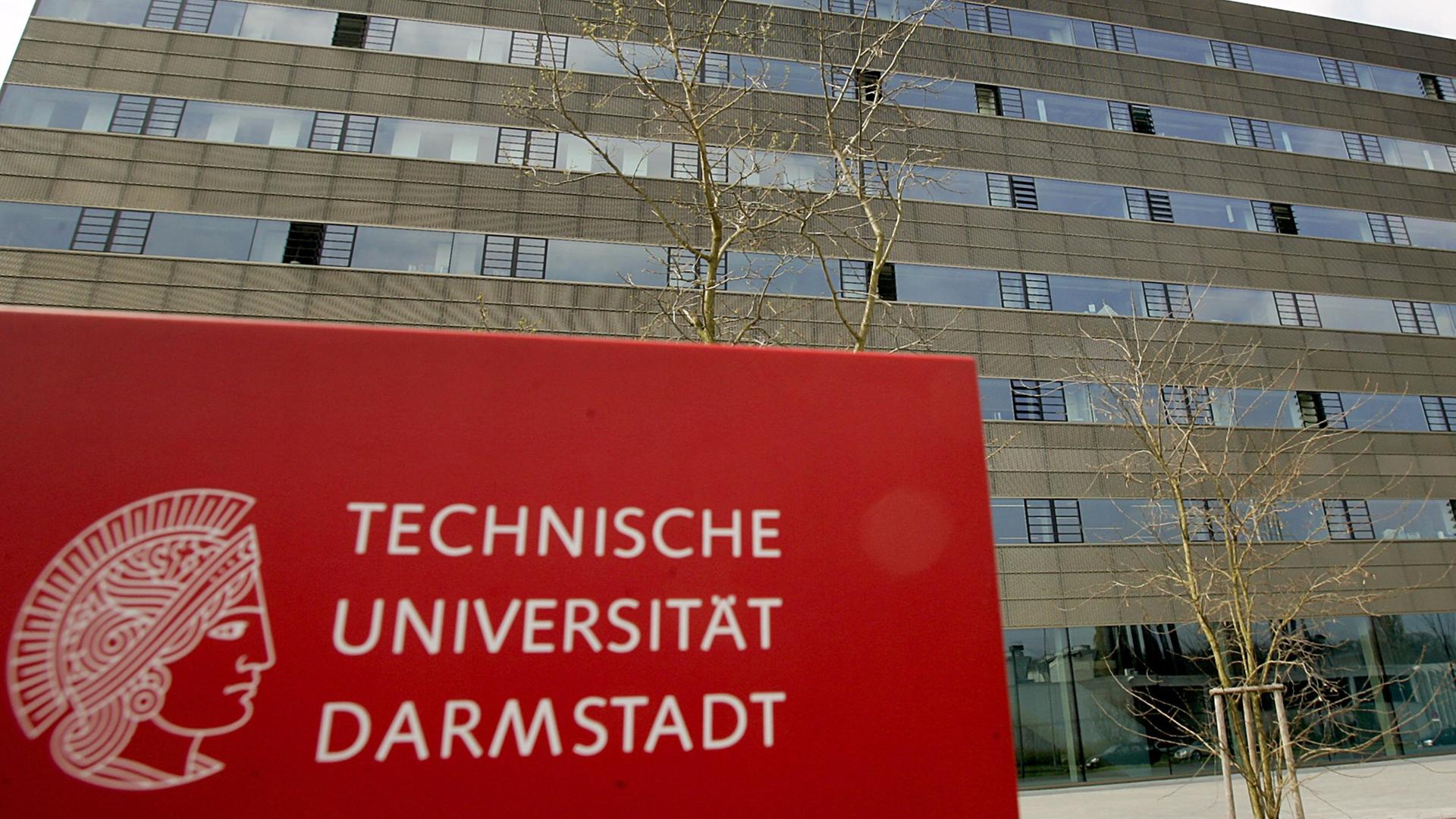 Rotes Schild mit der Aufschrift "Technische Universität Darmstadt" vor einem großen Gebäude.
