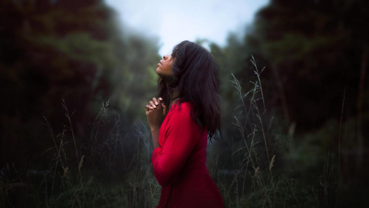 Eine Frau steht in einem Wald, hält die Hände vor der Brust zusammen und schaut in den Himmel. Eine Frau steht in einem Wald, hält die Hände vor der Brust zusammen und schaut in den Himmel.
