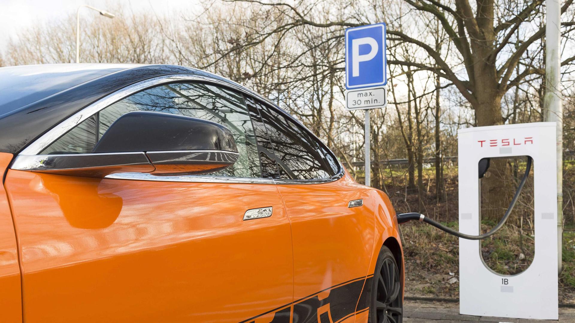 Ein orangefarbenes Elektro-Auto mit der Aufschrift "Tesla" ist an eine Ladestation angeschlossen.