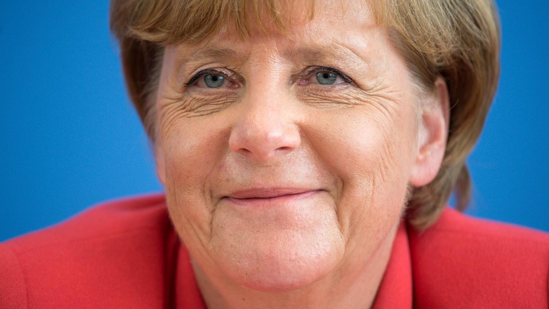 Auf dem Bild ist eine Nahaufnahme von Kanzlerin Merkel zu sehen. Sie blickt freundlich in die Kamera und lächelt leicht.