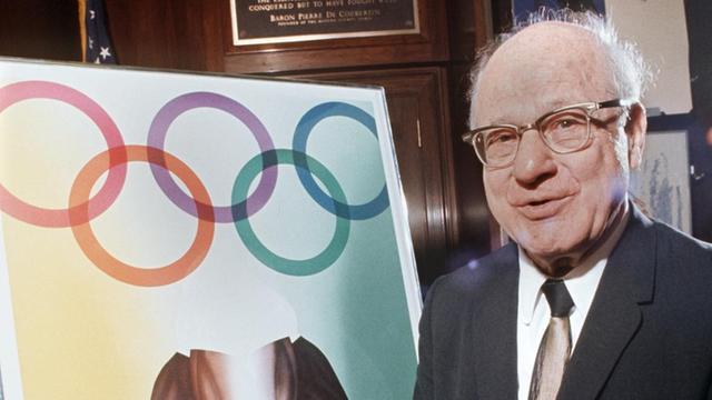 Der amerikanische Sportfunktionär und Präsident des Internationalen Olympischen Komitees (IOC), Avery Brundage, neben einem Plakat, das für die Olympischen Sommerspiele 1972 in München wirbt.